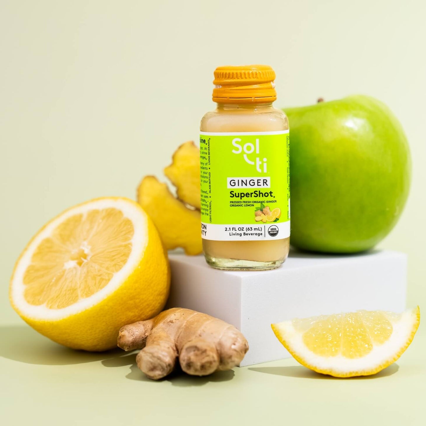 a bottle of GINGER SuperShot next to lemon slices, ginger root and a green apple
