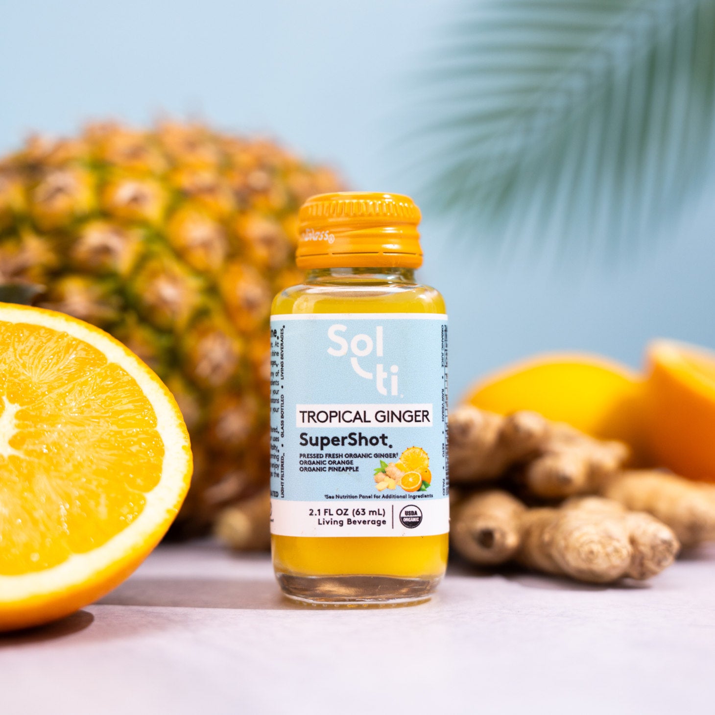 A TROPICAL GINGER SuperShot bottle next to orange slices, ginger root, and pineapple