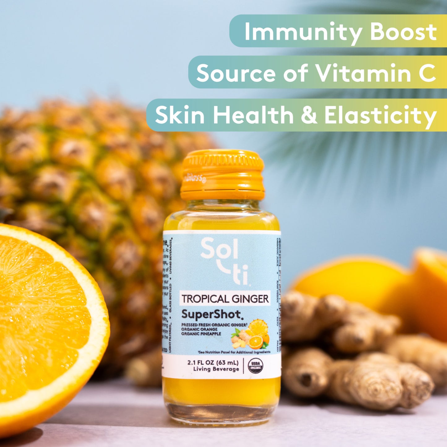 TROPICAL GINGER SuperShot bottle with front label on light blue background, with ginger root, lemon slice and pineapple, benefits text including Immunity boost, Source of Vitamin C and Skin Health & Elasticity